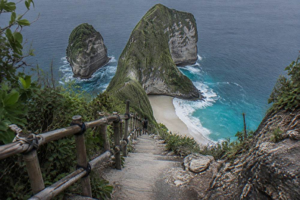 A steep stairway with a bamboo handrail dropping down the cliff toward Kelingking Beach