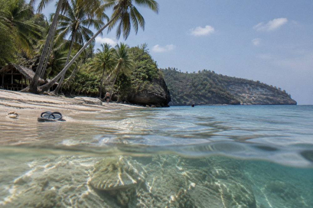Calm clear water over coral at Crystal Bay with a sandy beach and palm trees