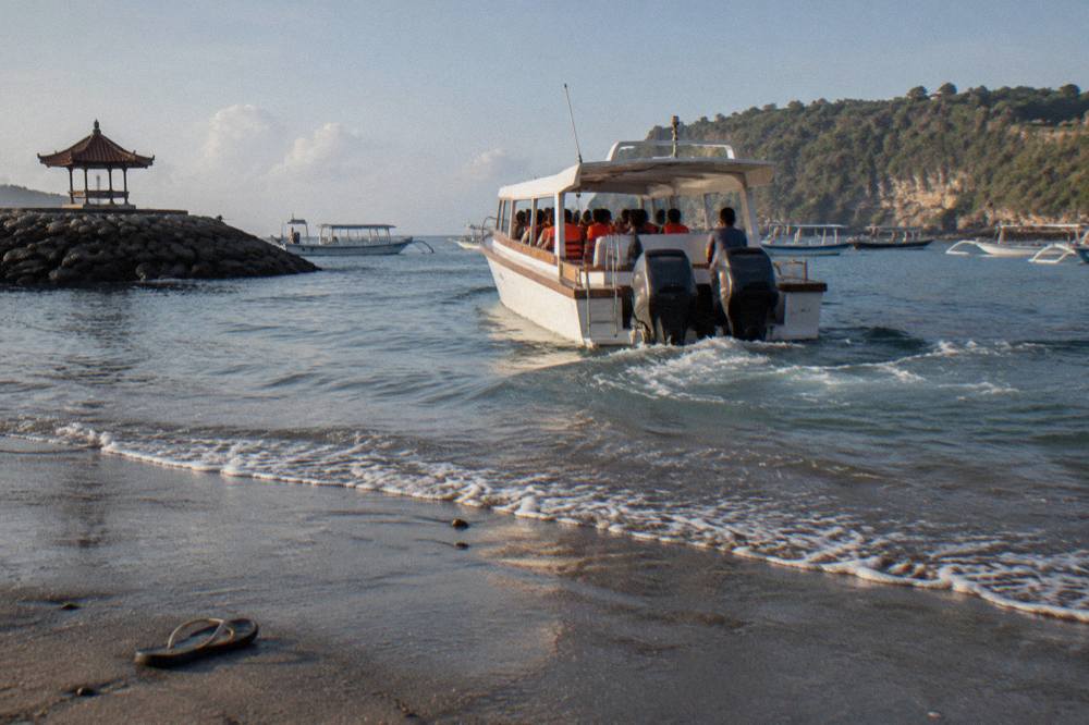 A white fast boat loaded with passengers pulling away from a sandy beach harbour in morning light