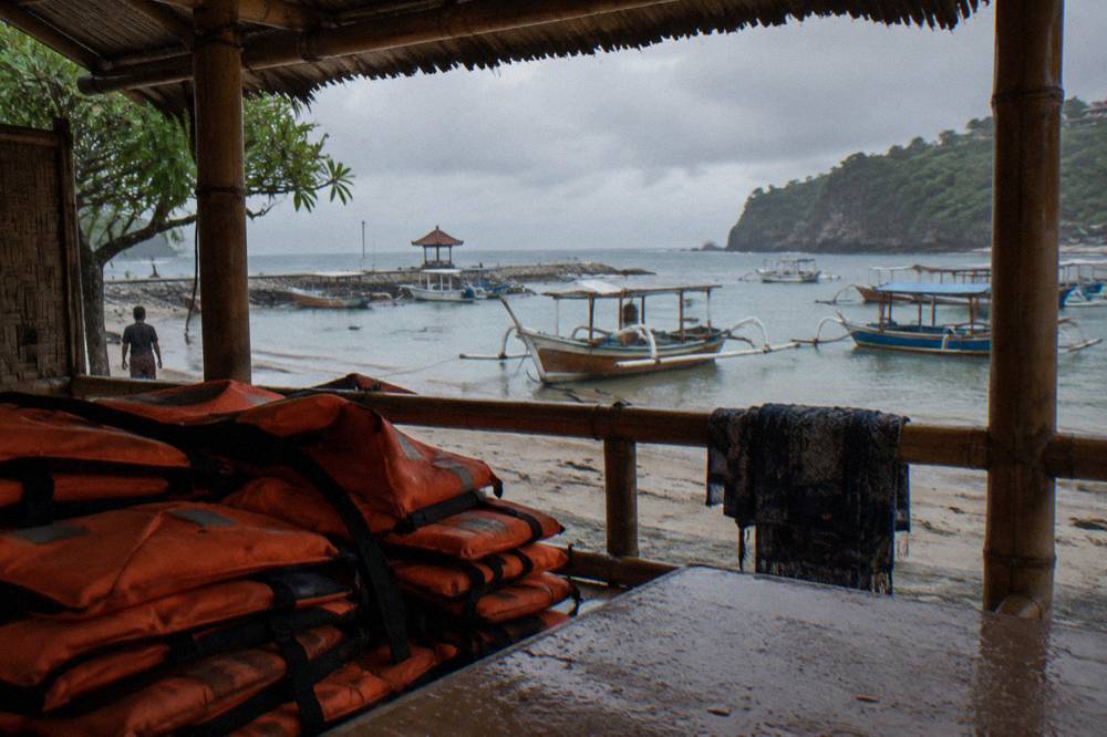 A ticket counter at a beachfront harbour with boats and orange life vests stacked beside it