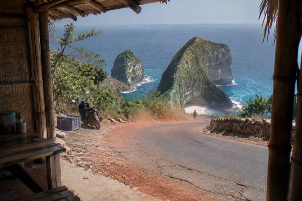 A quiet coastal road winding along the cliffs of western Nusa Penida in morning light
