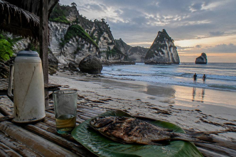 A simple beachfront dinner table with grilled fish at dusk on Nusa Penida